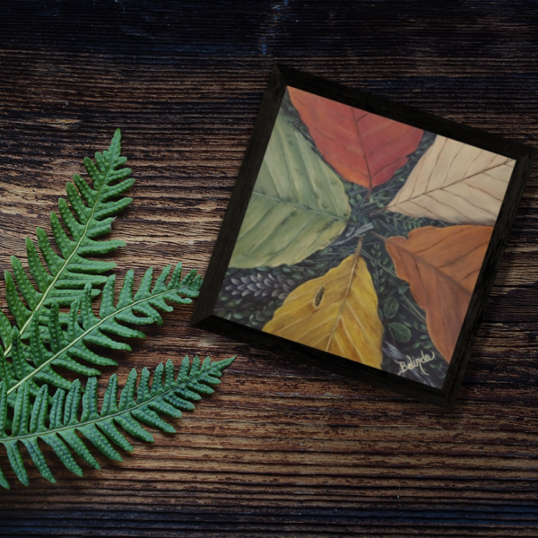 A mock-up photo of framed painting Falling Leaves by Be Designed Art Studio. This is a square painting in a black frame on a rustic wood background with a small fern.