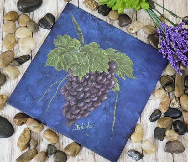 Painting of a lush grape cluster with green leaves against a deep blue background by artist Belinda Buckler